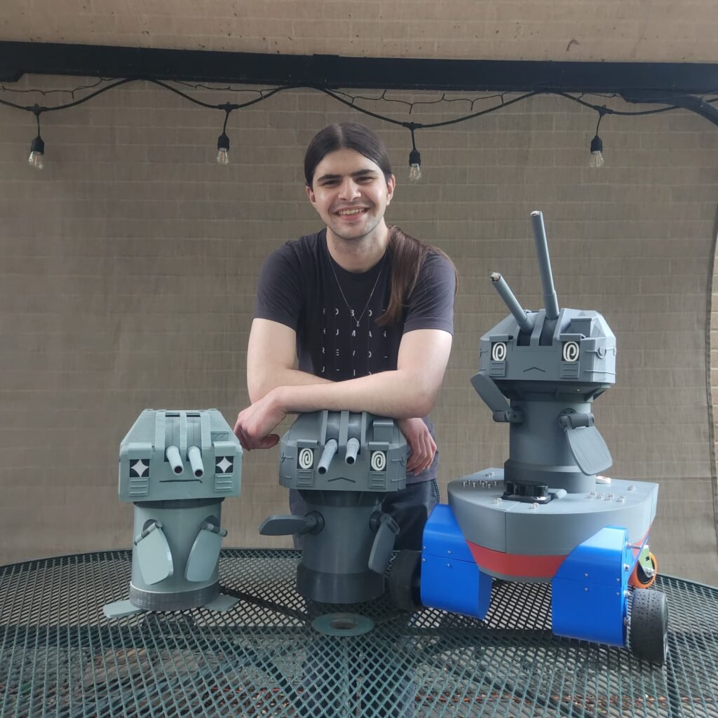 A young man smiles with several 3-d printed robots.